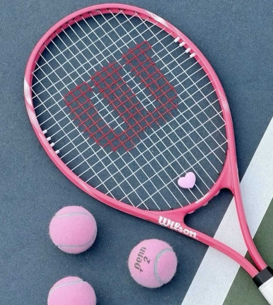 Rosa tennisracket och tillhörande utrustning fotograferad på tennisbana